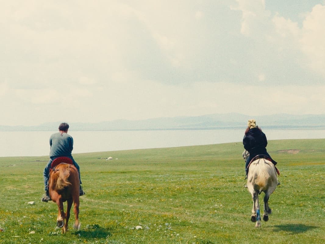 Deux cavaliers de dos traversant la steppe kirghize en direction du lac Son Koul