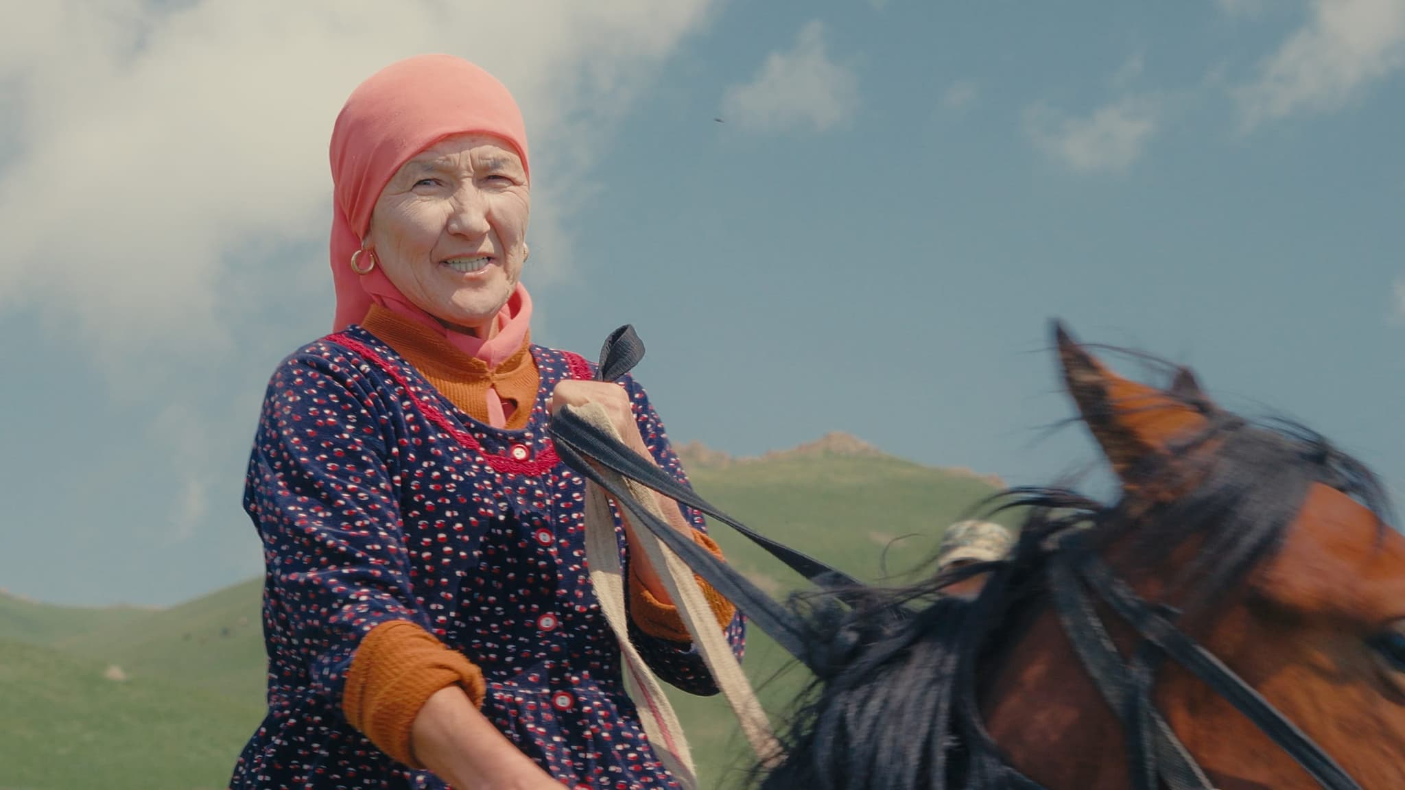 Une cavalière kirghize en foulard rose sur son cheval dans les montagnes autour du lac Son Kul